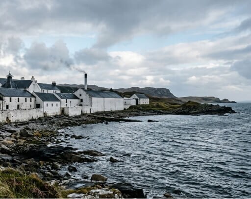 Islay header: het landschap van de Islay met een distilleerderij aan het water